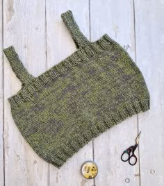 a knitted green sweater next to scissors and other craft supplies on a white wooden surface