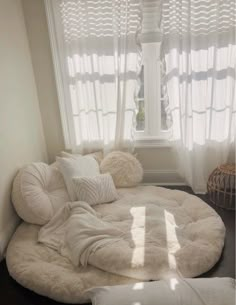 a large round bed in front of a window with white curtains and pillows on it