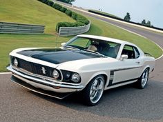 an old ford mustang is parked on the side of the road in front of a race track