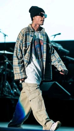 a man walking across a stage with his foot in the air while wearing sunglasses and a plaid jacket