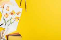 an arrangement of art supplies including watercolors, pencils and paper on a yellow background