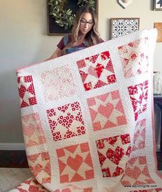 a woman holding up a red and white quilt