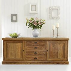 a white vase with flowers on top of a wooden dresser next to candles and pictures