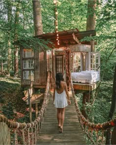 a woman walking across a wooden bridge in the middle of a forest with a tree house on it