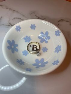 a white bowl with blue flowers and the letter b on it sitting on a marble table