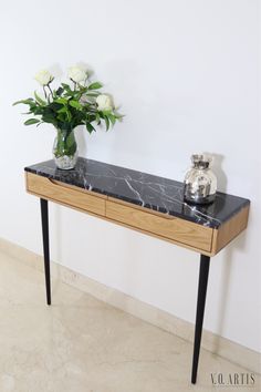 a marble top console table with black legs and white flowers in a vase on it