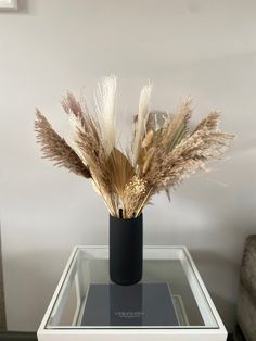 a black vase filled with dry grass on top of a table