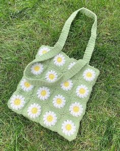 a crocheted bag sitting in the grass with daisies on it's side