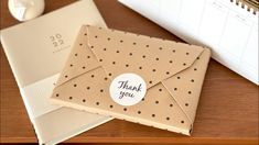 a brown envelope with a thank you sticker on it sitting next to a notepad