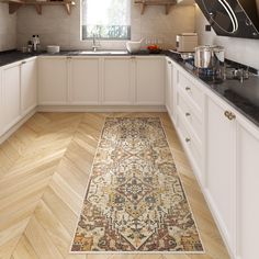 a kitchen with white cabinets and wooden floors, an area rug on the floor in front of the window