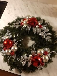 a christmas wreath with red and silver ornaments on it sitting on a marble counter top