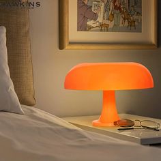 an orange lamp sitting on top of a bed next to a laptop computer and eyeglasses