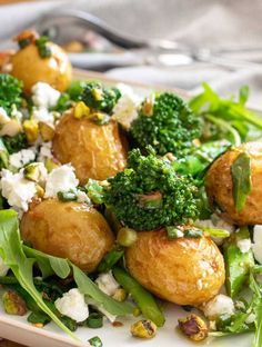 a white plate topped with potatoes, broccoli and feta cheese covered in sauce