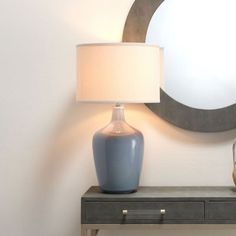 a blue vase sitting on top of a wooden table next to a lamp and mirror