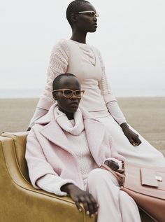 two women sitting on the back of a yellow car in front of an ocean and sky