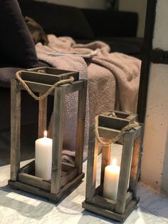 two wooden lanterns sitting on top of a floor next to each other with lit candles in them