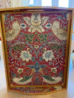 an intricately painted wooden frame with birds and flowers on red ground next to window