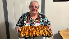 an older woman holding a tray full of hot dogs