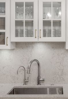 a kitchen with white cabinets and marble counter tops, silver faucet and stainless steel sink