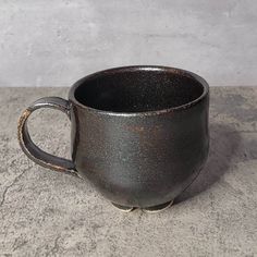 a black coffee cup sitting on top of a cement counter next to a white wall