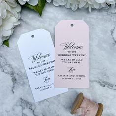 two wedding tags on top of a marble table next to some white and pink flowers