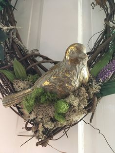 a bird statue sitting on top of a wreath with moss and flowers in the middle