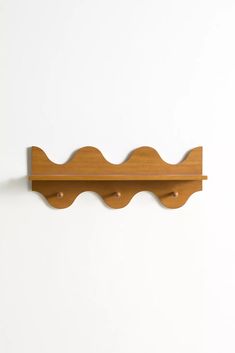 a wooden shelf mounted to the side of a white wall with two hooks on it