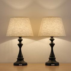 two lamps sitting on top of a wooden table next to each other with a white wall in the background