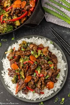 beef and broccoli stir fry on rice in a skillet with chopsticks