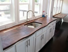 a kitchen with white cabinets and wood counter tops in front of two windows, along with a stainless steel faucet