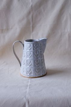 a white ceramic pitcher sitting on top of a tablecloth covered floor next to a wall