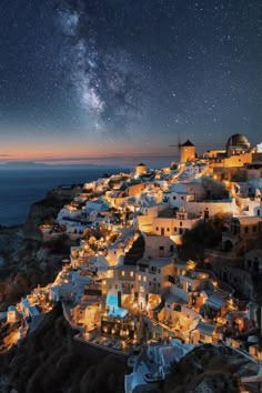 the night sky is filled with stars and white buildings on top of a hill next to the ocean