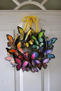 a wreath made out of colorful butterflies hanging from a white door with a yellow ribbon