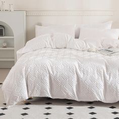 a bed with white comforter and pillows in a small room next to a book shelf