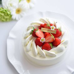 a white cake topped with strawberries on top of a plate next to some flowers