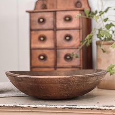 a wooden bowl sitting on top of a table next to a dresser and potted plant