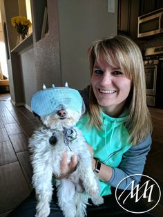 a woman holding a small white dog wearing a hat