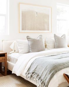 a bed with white linens and pillows in a bedroom next to a painting on the wall