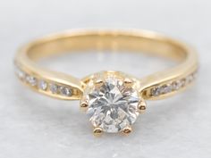 a yellow gold engagement ring with an oval cut diamond in the center and side stones around the band