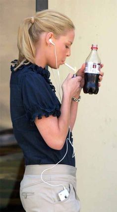 a woman with headphones is holding a soda bottle and listening to earbuds