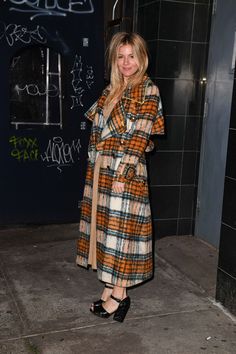 a woman standing in front of a black wall wearing a plaid coat and matching heels