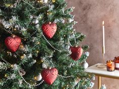 a christmas tree decorated with red heart ornaments and candles in front of a marble wall