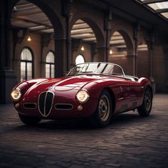 a red sports car is parked in an old building with arched windows and brick flooring