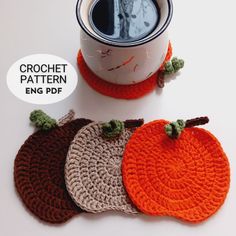 three crocheted pumpkin coasters sitting next to a coffee cup