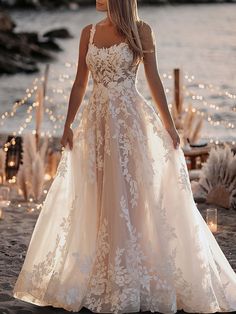 a woman in a wedding dress standing on the beach with candles lit up behind her