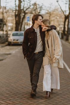 a man and woman are walking down the street together, one is kissing the other's forehead