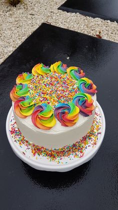 a white cake topped with rainbow sprinkles on top of a black table