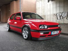 a red car parked in front of a building with graffiti on the wall behind it