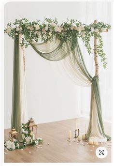 a wedding arch decorated with greenery and white flowers on the floor next to candles