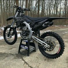 a dirt bike parked on top of a stand in the middle of a road next to trees